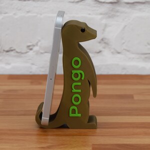 K&ouml;nnte beinhalten: Ein gr&uuml;ner und brauner Telefonst&auml;nder in Form eines Erdm&auml;nnchens mit dem Wort "Pongo" auf der Seite. Der St&auml;nder h&auml;lt ein wei&szlig;es Smartphone.