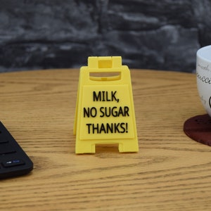 May include: Yellow caution sign with black text that reads "Milk, No Sugar Thanks!"