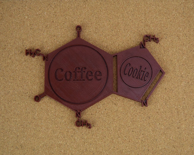 Puede incluir: Un modelo 3D impreso en marr&oacute;n de una estructura qu&iacute;mica con las palabras "Coffee" y "Cookie" en el centro de cada anillo.