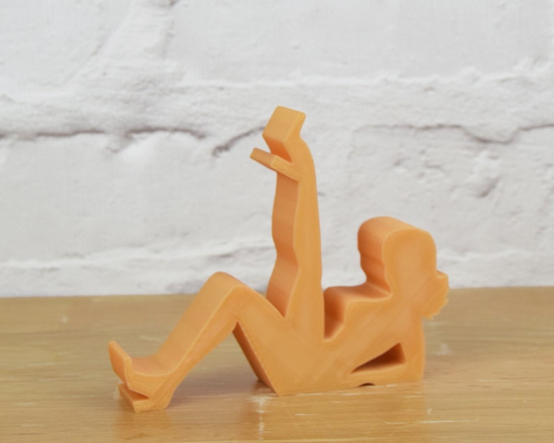 May include: A peach-colored, abstract sculpture of a person in a sitting position with one leg raised. The sculpture is made of a smooth, matte material.