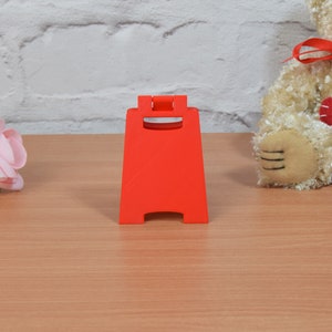 Op de afbeelding: Een felrood, plastic A-frame bord met afgeronde hoeken en een vlak oppervlak. Het bord staat op een houten tafel.