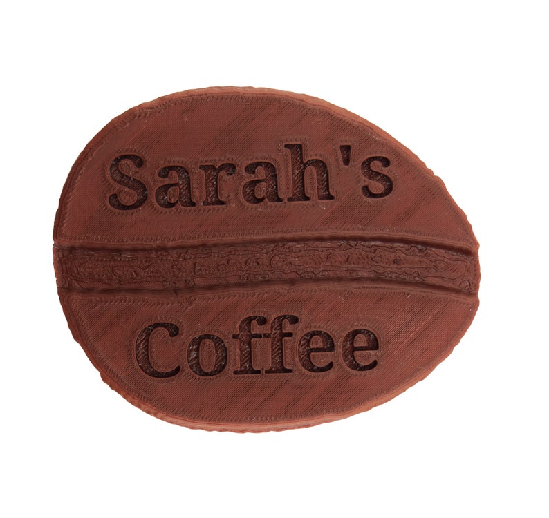 May include: A brown ceramic coffee bean with the text "Sarah's Coffee" embossed on the surface.