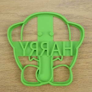 May include: Green plastic cookie cutter shaped like a cartoon character with the word "HARRY" written across the front.