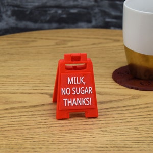 Może przedstawiać: Czerwony plastikowy znak z napisem "Milk, No Sugar Thanks!" na drewnianym stole.
