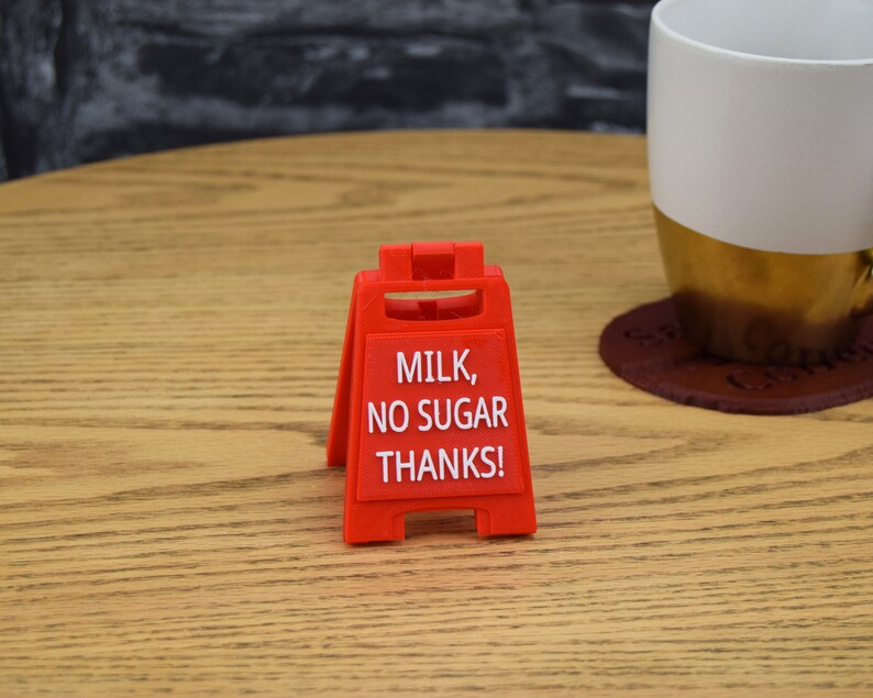 Może przedstawiać: Czerwony plastikowy znak z napisem "Milk, No Sugar Thanks!" na drewnianym stole.