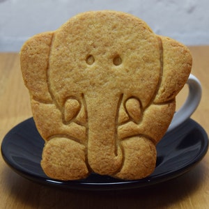 May include: A light brown cookie shaped like an elephant, with a small black saucer underneath.