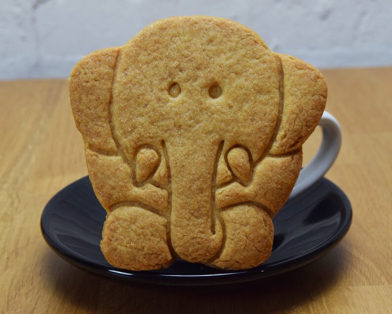 May include: A light brown cookie shaped like an elephant, with a small black saucer underneath.