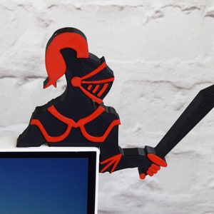 Op de afbeelding: Een 3D-geprint zwart en rood ridderfiguur dat een zwaard vasthoudt. De ridder draagt een helm en harnas. Het figuur staat op een wit oppervlak.