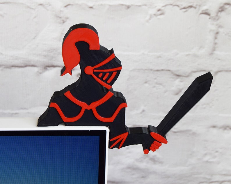Op de afbeelding: Een 3D-geprint zwart en rood ridderfiguur dat een zwaard vasthoudt. De ridder draagt een helm en harnas. Het figuur staat op een wit oppervlak.