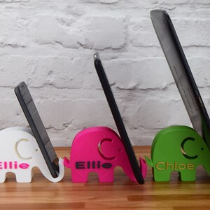 May include: Three 3D printed elephant phone and tablet stands. The stands are white, pink, and green. The white stand has the name "Ellie C." printed on it. The pink stand has the name "Ellie C." printed on it. The green stand has the name "Chloe C." printed on it.