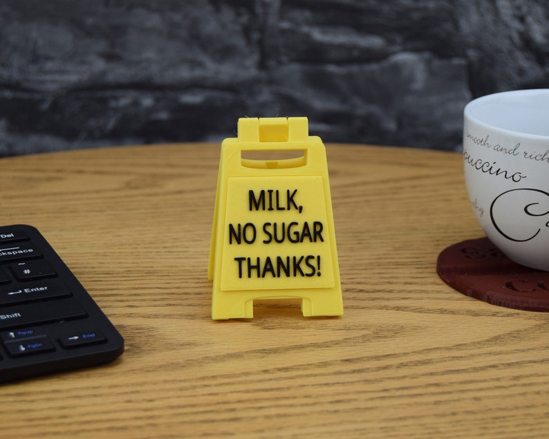 May include: Yellow caution sign with black text that reads "Milk, No Sugar Thanks!"
