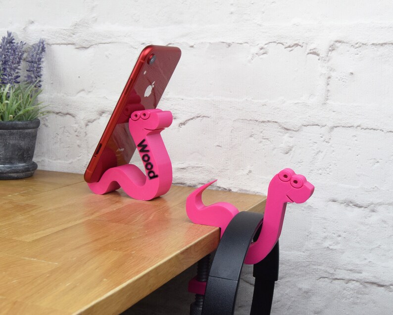 May include: Two pink worm-shaped phone and headphone holders. The phone holder has a red phone propped against it and the word "Wood" printed on the side.