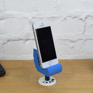May include: A blue 3D printed phone stand shaped like a hand holding a phone. The stand has the name "Jason" printed on the base.