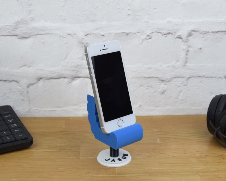 May include: A blue 3D printed phone stand shaped like a hand holding a phone. The stand has the name "Jason" printed on the base.