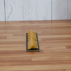 May include: A rectangular black tray holds several triangular, yellow-orange cheese wedges. The cheese pieces are neatly arranged, showcasing their shape and color. The tray sits on a wooden surface.