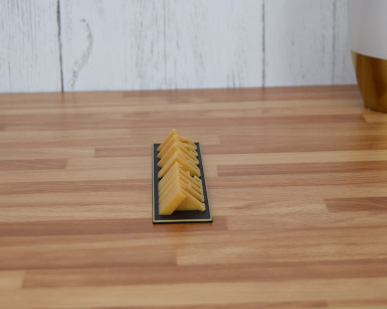 May include: A rectangular black tray holds several triangular, yellow-orange cheese wedges. The cheese pieces are neatly arranged, showcasing their shape and color. The tray sits on a wooden surface.