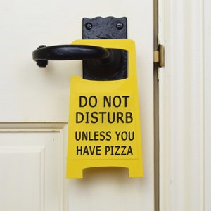 Op de afbeelding: Geel deurschild met zwarte tekst die zegt "Niet storen, tenzij je pizza hebt".