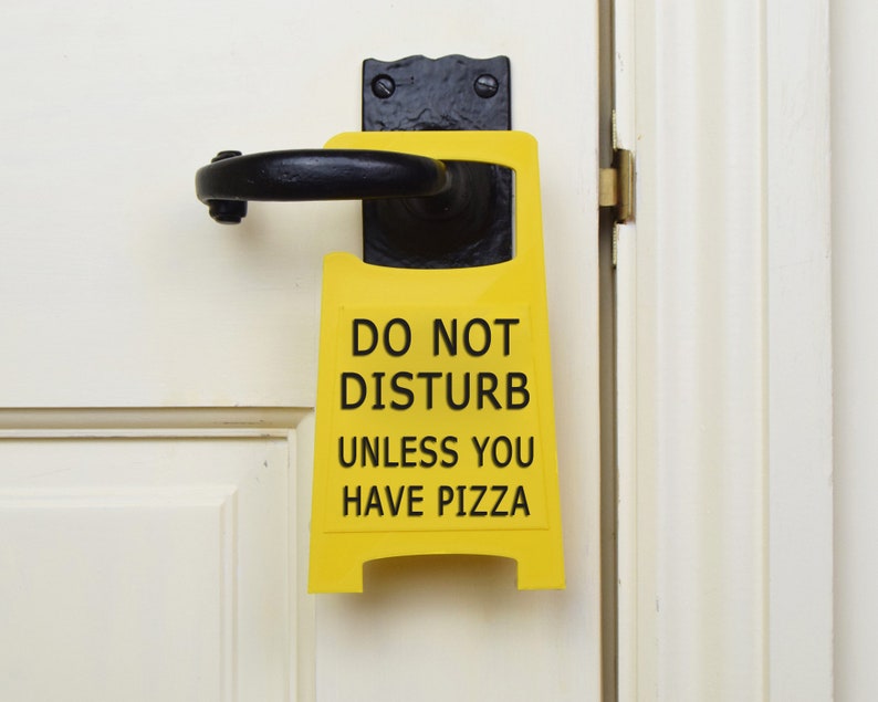 Op de afbeelding: Geel deurschild met zwarte tekst die zegt "Niet storen, tenzij je pizza hebt".