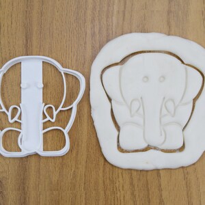 May include: Two white plastic cookie cutters shaped like elephants. The cutter on the left is a simple outline of an elephant, while the cutter on the right is a more detailed outline of an elephant with a trunk, ears, and legs.
