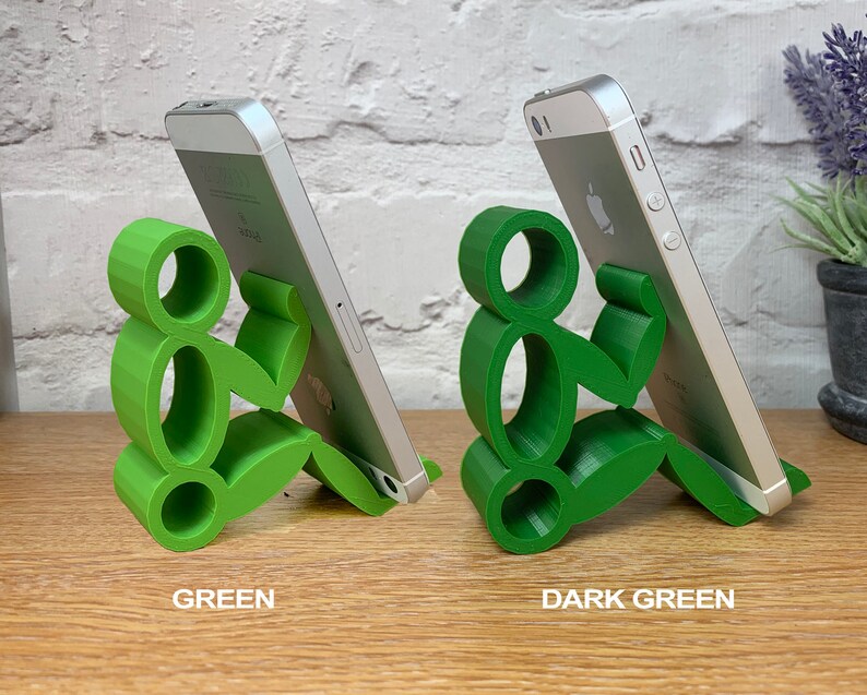 May include: Two phone stands made of green plastic, shaped like a person sitting down. The stand on the left is a lighter shade of green, while the stand on the right is a darker shade of green.