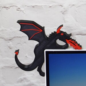 May include: A black and red dragon-shaped corner shelf decor. The dragon has red accents on its wings, eyes, and the fire it breathes. The shelf is designed to fit over the corner of a desk or shelf.
