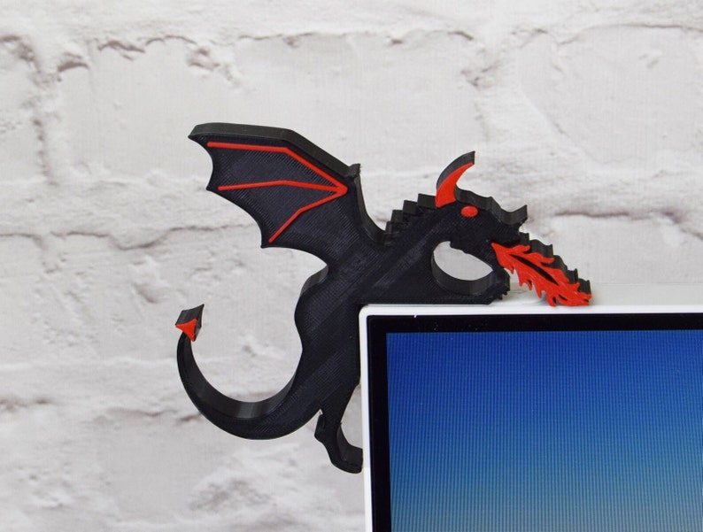 May include: A black and red dragon-shaped corner shelf decor. The dragon has red accents on its wings, eyes, and the fire it breathes. The shelf is designed to fit over the corner of a desk or shelf.