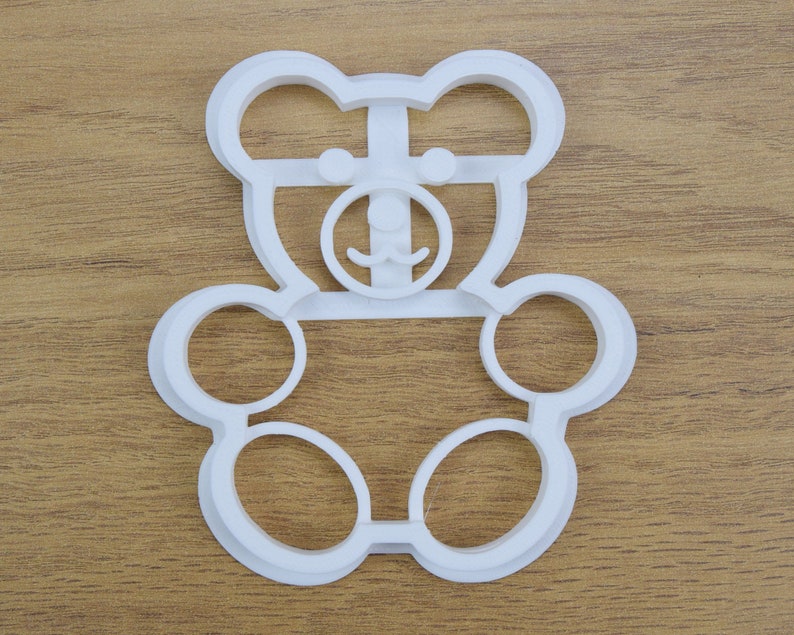 May include: White plastic cookie cutter shaped like a teddy bear with a simple face.