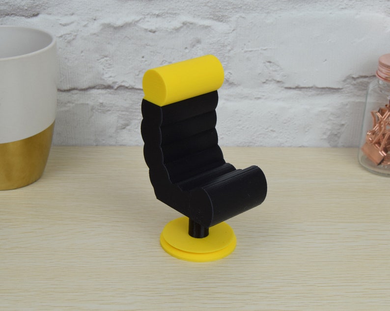 May include: A black and yellow 3D printed miniature chair with a rounded back and a swivel base.