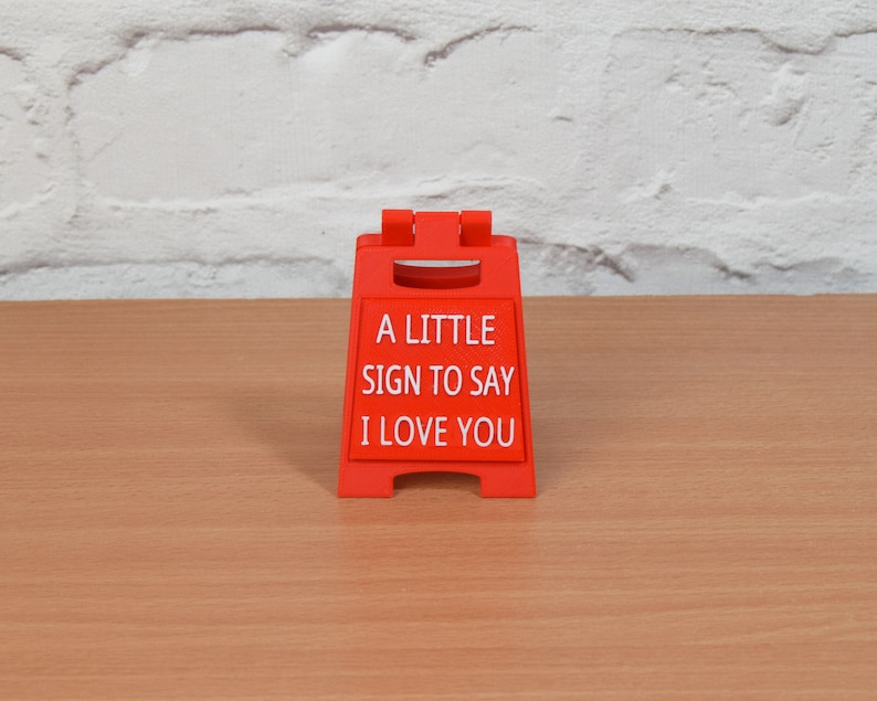 Op de afbeelding: Een rood plastic bord met de tekst "A little sign to say I love you".
