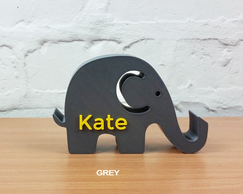 Pode incluir: Uma figura de elefante cinza com uma etiqueta de nome amarela que diz "Kate".