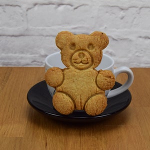 May include: A brown teddy bear cookie on a black saucer with a white teacup behind it.