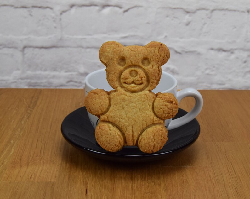 May include: A brown teddy bear cookie on a black saucer with a white teacup behind it.