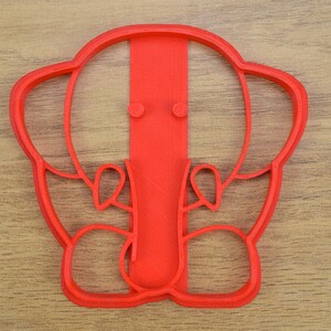 May include: Red plastic cookie cutter shaped like an elephant with a trunk and ears.