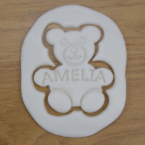 Puede incluir: Cortador de galletas de pl&aacute;stico blanco con forma de osito de peluche con el nombre Amelia recortado en el interior.