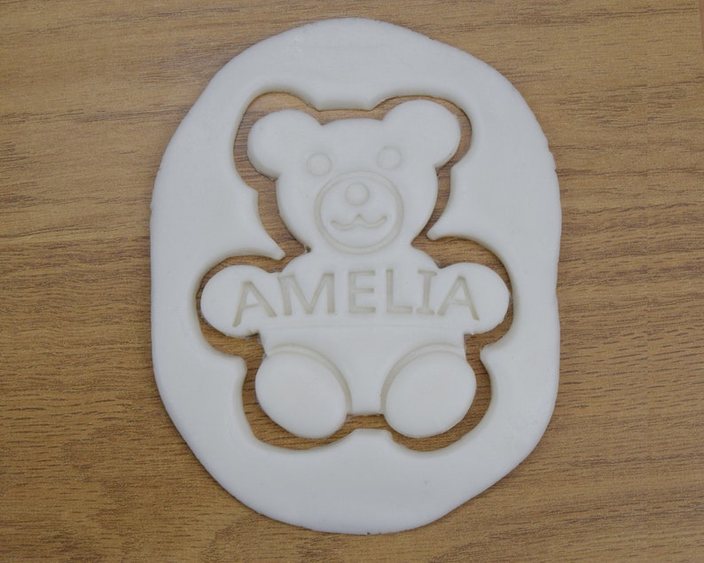 Puede incluir: Cortador de galletas de pl&aacute;stico blanco con forma de osito de peluche con el nombre Amelia recortado en el interior.