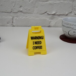 May include: Yellow warning sign with black text that reads "WARNING! I NEED COFFEE!"