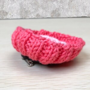 May include: A pink knitted flower brooch with a silver clasp. The flower is made with a textured knit pattern.
