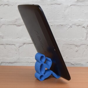 May include: A blue 3D printed stand shaped like a person holding a black tablet with the word "nexus" printed on the back.