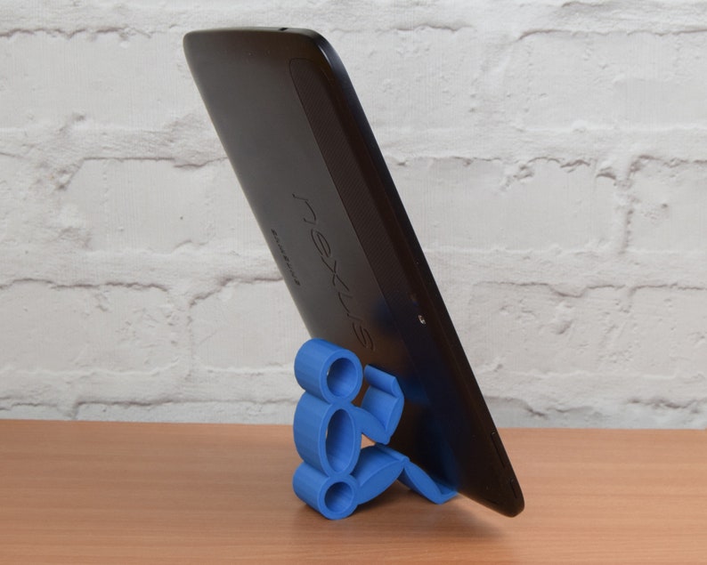 May include: A blue 3D printed stand shaped like a person holding a black tablet with the word "nexus" printed on the back.