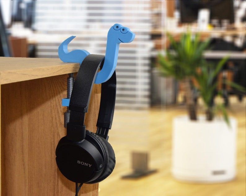 May include: A blue plastic headphone holder shaped like a cartoon snake with a clamp to attach to a desk or shelf. A pair of black Sony headphones are hanging from the holder.