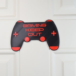 以下が含まれることがあります： 「Gaming Keep Out」というテキストが書かれた黒と赤のゲームコントローラーのサイン。