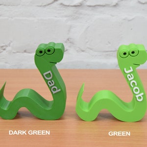 May include: Two 3D printed green snake-shaped doorstops. The snake on the left is dark green and says "Dad". The snake on the right is a lighter green and says "Jacob".