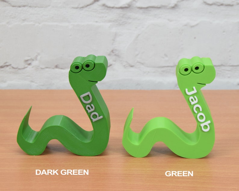 May include: Two 3D printed green snake-shaped doorstops. The snake on the left is dark green and says "Dad". The snake on the right is a lighter green and says "Jacob".