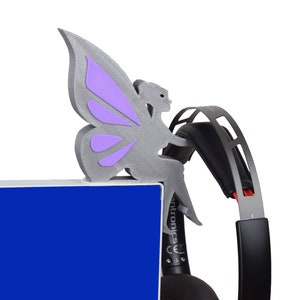 K&ouml;nnte beinhalten: Eine graue, 3D-gedruckte Feenfigur mit lila Fl&uuml;geln, die auf einem schwarzen Headset sitzt. Die Fee sitzt auf einer blauen Oberfl&auml;che.
