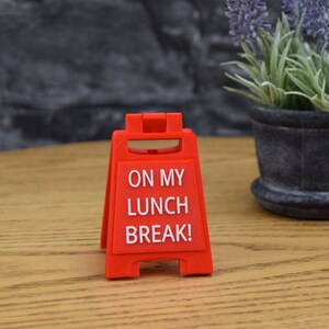 May include: Red plastic sign with the text "ON MY LUNCH BREAK!" on a wooden surface.