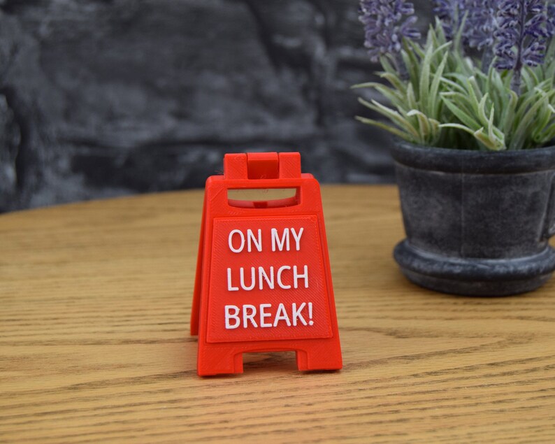 May include: Red plastic sign with the text "ON MY LUNCH BREAK!" on a wooden surface.
