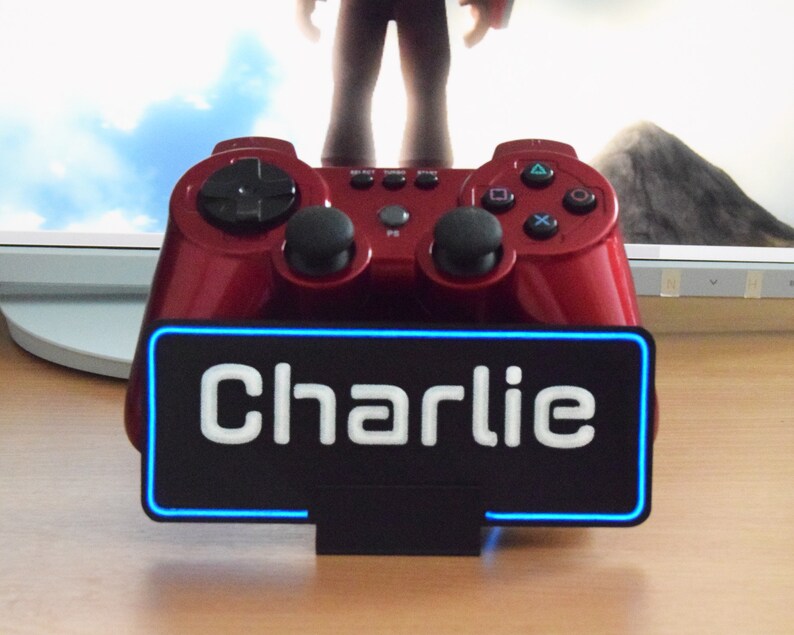 Pu&ograve; includere: Un controller per videogiochi rosso con una base nera e un cartello al neon blu che dice "Charlie".