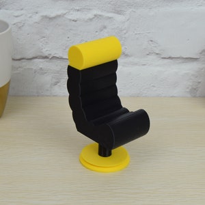 May include: A black and yellow 3D printed miniature chair with a rounded back and a swivel base.