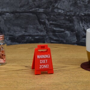 May include: Red warning sign with the text "WARNING! DIET ZONE!" on a wooden table.