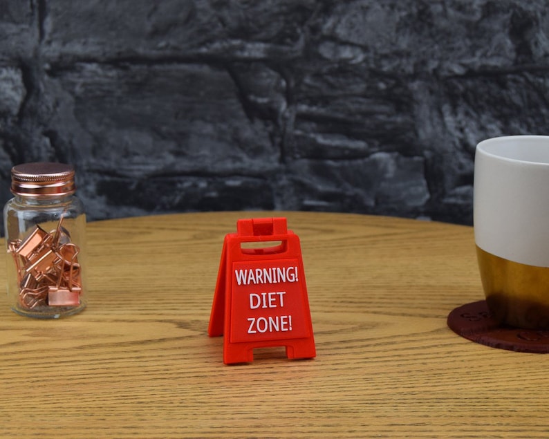 May include: Red warning sign with the text "WARNING! DIET ZONE!" on a wooden table.